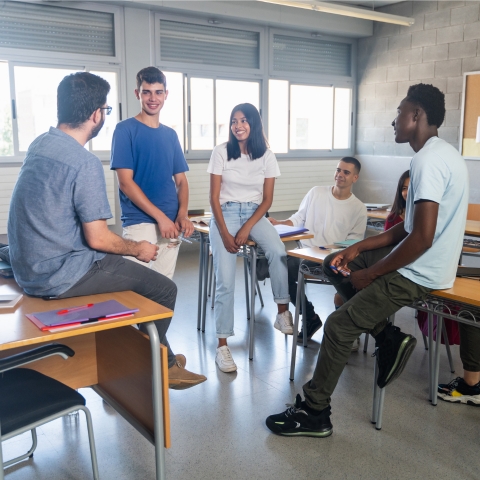 Group of smiling high school students talk to a teacher