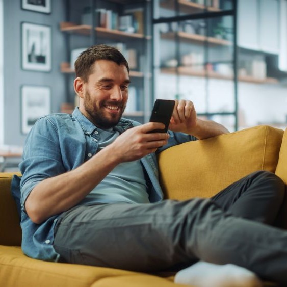 smiling man sitting on couch at home using smartphone