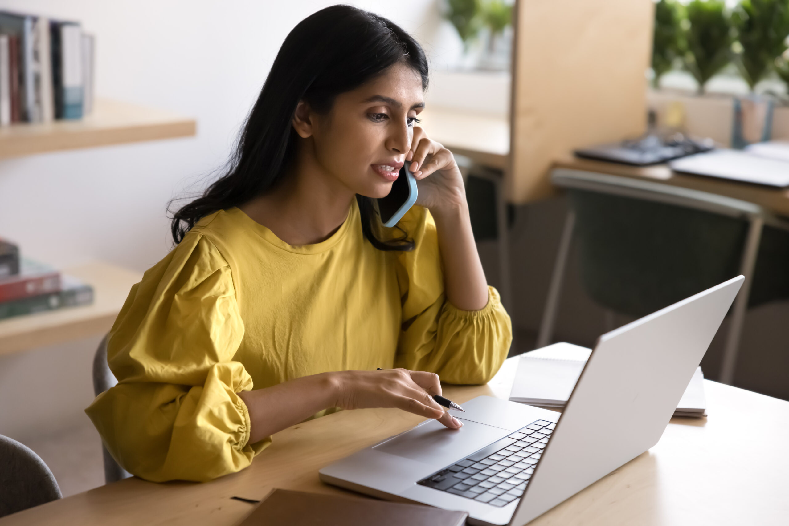 Serious Indian woman speak on phone while working on laptop Stressed man looking at computer screen